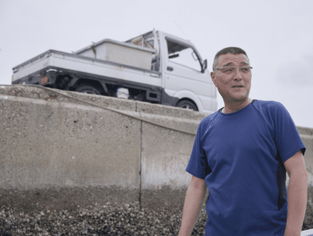 キャリイを背に船上に立つ漁師
